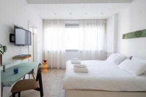 A hotel room with a bed, a desk with a chair, a television, and a window with curtains. - 3BR + 3 Baths near Gordon Beach by SeaNRent (Tel Aviv)