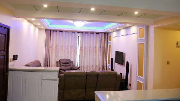 Un salon comprenant un canapé, un fauteuil, un téléviseur fixé au mur et un luminaire suspendu au plafond.