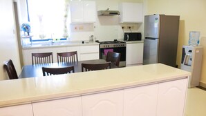 Une cuisine avec des meubles blancs, une cuisinière, un réfrigérateur et un distributeur d’eau.