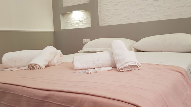Una cama bien hecha con ropa de cama rosa, almohadas blancas y toallas enrolladas.