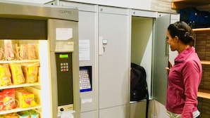 Máquina expendedora llena de aperitivos y bebidas, un teclado y un aviso en la puerta.