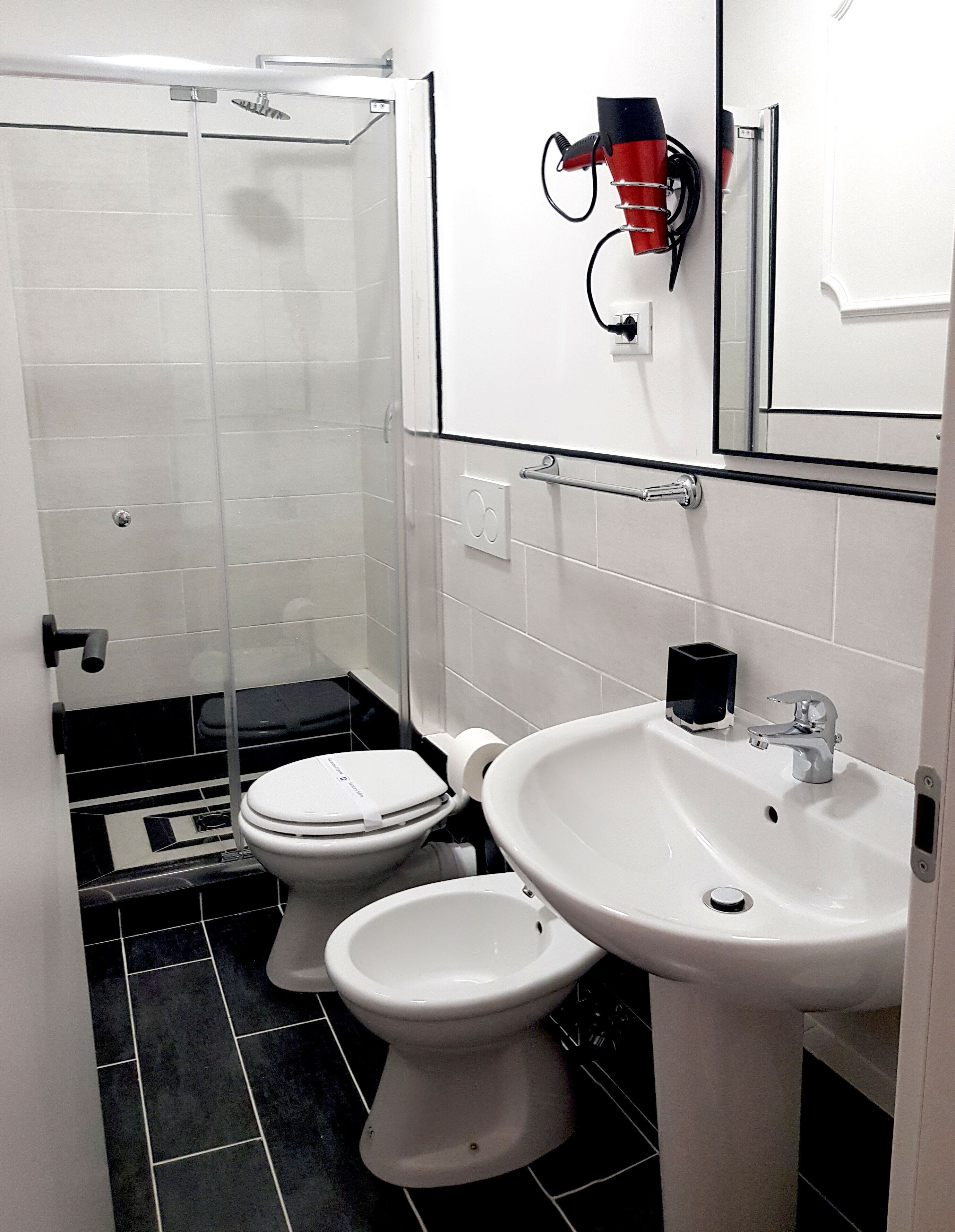 Ein Badezimmer mit zwei Toiletten, einem Waschbecken, einem Spiegel und einer Dusche.