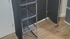 Un estante metálico con tapa negra, que incluye varias repisas y un perchero.