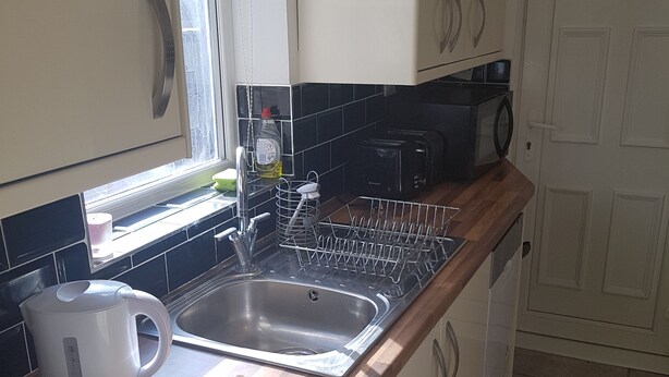 Una cocina con un lavamanos de acero inoxidable, una tetera, un microondas y un escurreplatos.