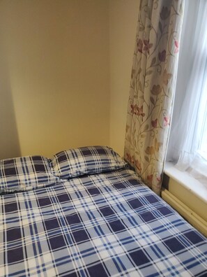 Una cama con colcha escocesa y cortinas florales.