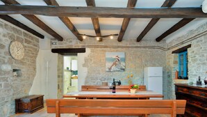 A rustic kitchen with a wooden bench, stone walls, and a painting of a woman on the wall.