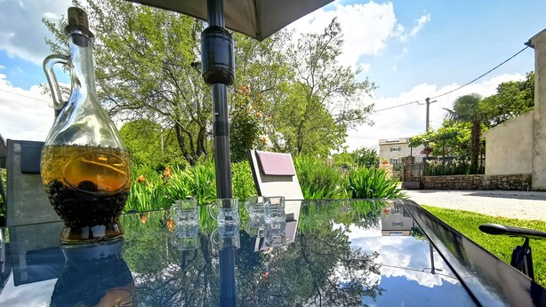 A glass table with a bottle and glasses, reflecting trees and sky.