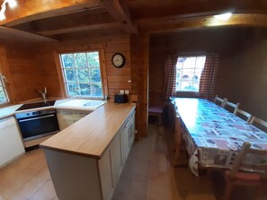 Eine Holzhütte mit einer Küche, die ein Spülbecken, einen Herd und Schränke sowie einen Essbereich mit Tisch und Stühlen bietet.