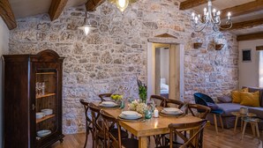 Un comedor con pared de piedra, vigas de madera en el techo, una araña y una mesa para cuatro.