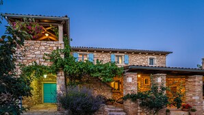 Un edificio de piedra con una puerta verde, un balcón con plantas y una entrada bien iluminada.