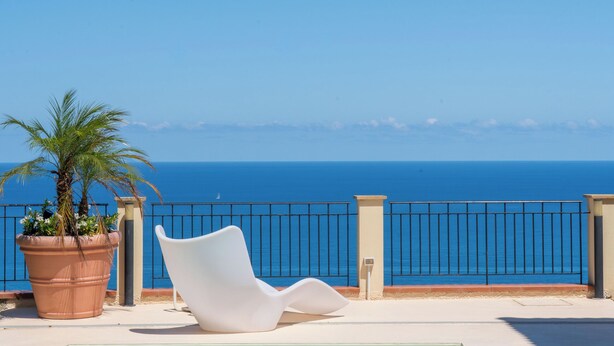 Una piscina con vista chiara sul mare, una sedia bianca e una pianta in vaso.