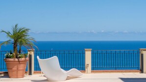 Un balcone con una sedia bianca e un vaso in terracotta di grandi dimensioni con una palma.