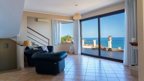 Un soggiorno spazioso con un'ampia porta-finestra scorrevole che dà su un balcone con vista sull'oceano.
