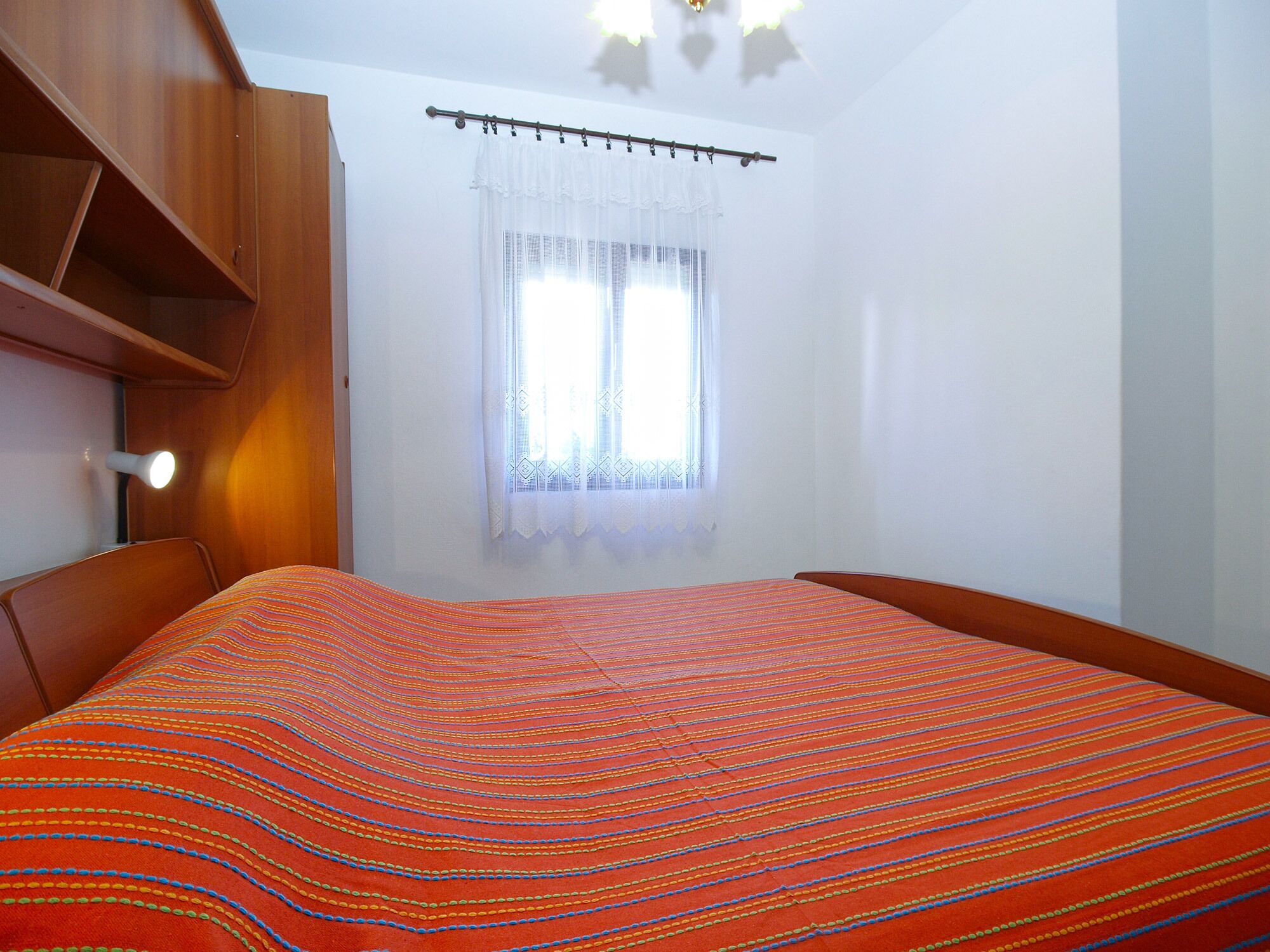 A bedroom with a wooden bed frame, a white curtain, and a window with a view.