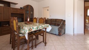 A dining area with a table set for four, surrounded by wooden chairs. A floral tablecloth covers the table, and a cabinet with glass doors is visible in the background. - Apartment 1858/22636 (Istria - Valbandon), 1000m from the beach (Valbandon)