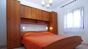 A bedroom with a wooden bed frame, a built-in wardrobe, and a window with curtains. - Apartment 1858/22636 (Istria - Valbandon), 1000m from the beach (Valbandon)