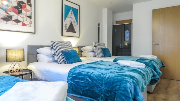A hotel room with a bed, a bedside table, a lamp, and a wardrobe. - Tudors eSuites Birmingham Canalside Apartments (Birmingham)