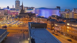A cityscape at dusk with illuminated buildings, including a distinctive dome-shaped structure with blue lighting. - Tudors eSuites Birmingham Canalside Apartments (Birmingham)