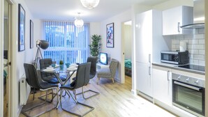 A modern kitchen with a microwave, oven, and white cabinets. There is a dining area with a glass table and chairs. - Tudors eSuites Birmingham Canalside with Gated Parking (Birmingham)