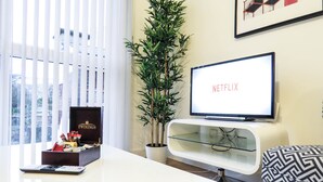 A modern living room with a television displaying 'NETFLIX', a potted plant, a wooden coffee table, and a framed picture on the wall. - Tudors eSuites Birmingham Canalside with Gated Parking (Birmingham)