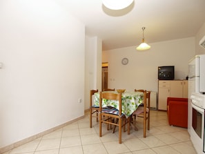 Una cocina compacta con una mesa de comedor, sillas, un reloj, un televisor y un refrigerador.
