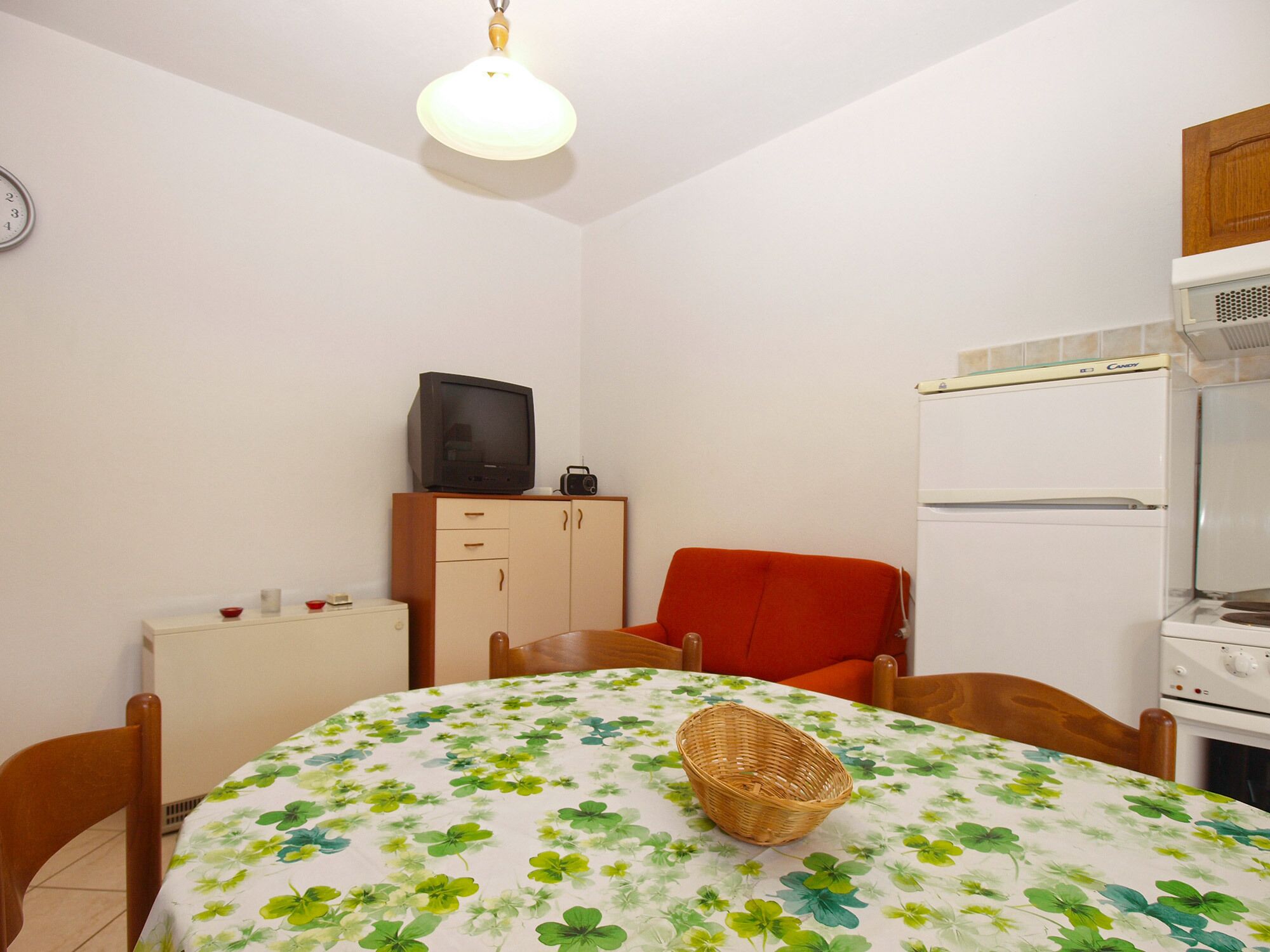 Una cocina pequeña y funcional con una mesa de comedor, sillas, un refrigerador, estufa y un televisor sobre un mueble.