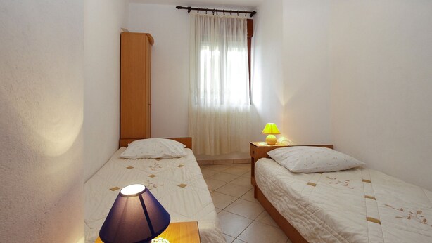 A small, well-lit bedroom with two single beds, a wooden wardrobe, a bedside table with a lamp, and a window with sheer curtains. - Apartment 1858/22637 (Istria - Valbandon), 1000m from the beach (Valbandon)