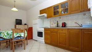 A compact kitchen with wooden cabinets, a white stove, a sink, and a dining area with a table and chairs. - Apartment 1858/22637 (Istria - Valbandon), 1000m from the beach (Valbandon)