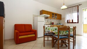 A compact kitchen with wooden cabinets, a white refrigerator, a dining table with chairs, and a red sofa. - Apartment 1858/22637 (Istria - Valbandon), 1000m from the beach (Valbandon)