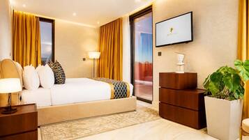 A hotel room with a bed, bedside tables, a TV, a desk, and a large plant.