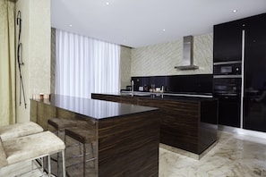 Una cuina moderna amb una illa central, tamborets de bar, microones, forn i una campana extractora d'acer inoxidable.