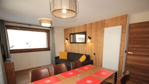 Un comedor con una mesa de madera, individuales rojos, sillas de cuero marrón, una pared de madera con un espejo y una ventana con cortinas.