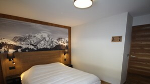 Una habitación de hotel con una cama grande, cabecera de madera, una pintura de montañas y una puerta de madera.