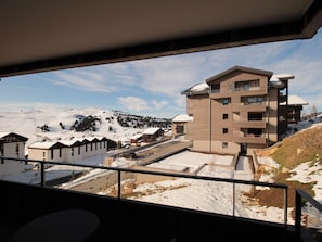 Ein modernes Gebäude mit mehreren Stockwerken und flachem Dach, umgeben von schneebedeckten Hügeln und wolkenlosem Himmel.