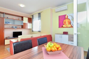 Un salon moderne avec un canapé, une table à manger ornée de fruits, un téléviseur et une statue de Bouddha.