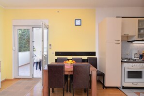Un coin repas avec une table dressée pour quatre personnes, une cuisine équipée d’une cuisinière et d’un four, et une porte donnant sur un espace extérieur.