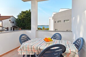 Ein Balkon mit Tisch für zwei Personen, mit einer Obstschale und einer karierten Tischdecke.