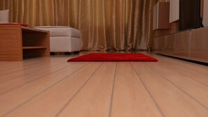 Een kamer met een houten vloer, een rood kleed, een witte bank en een houten kast.