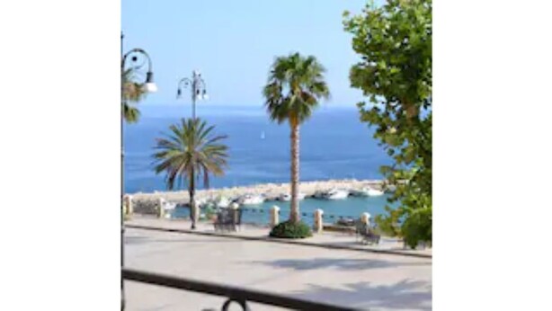 A coastal promenade with a view of the sea, palm trees, and a row of beachside buildings. - Agorà Panoramic Rooms (Sciacca)