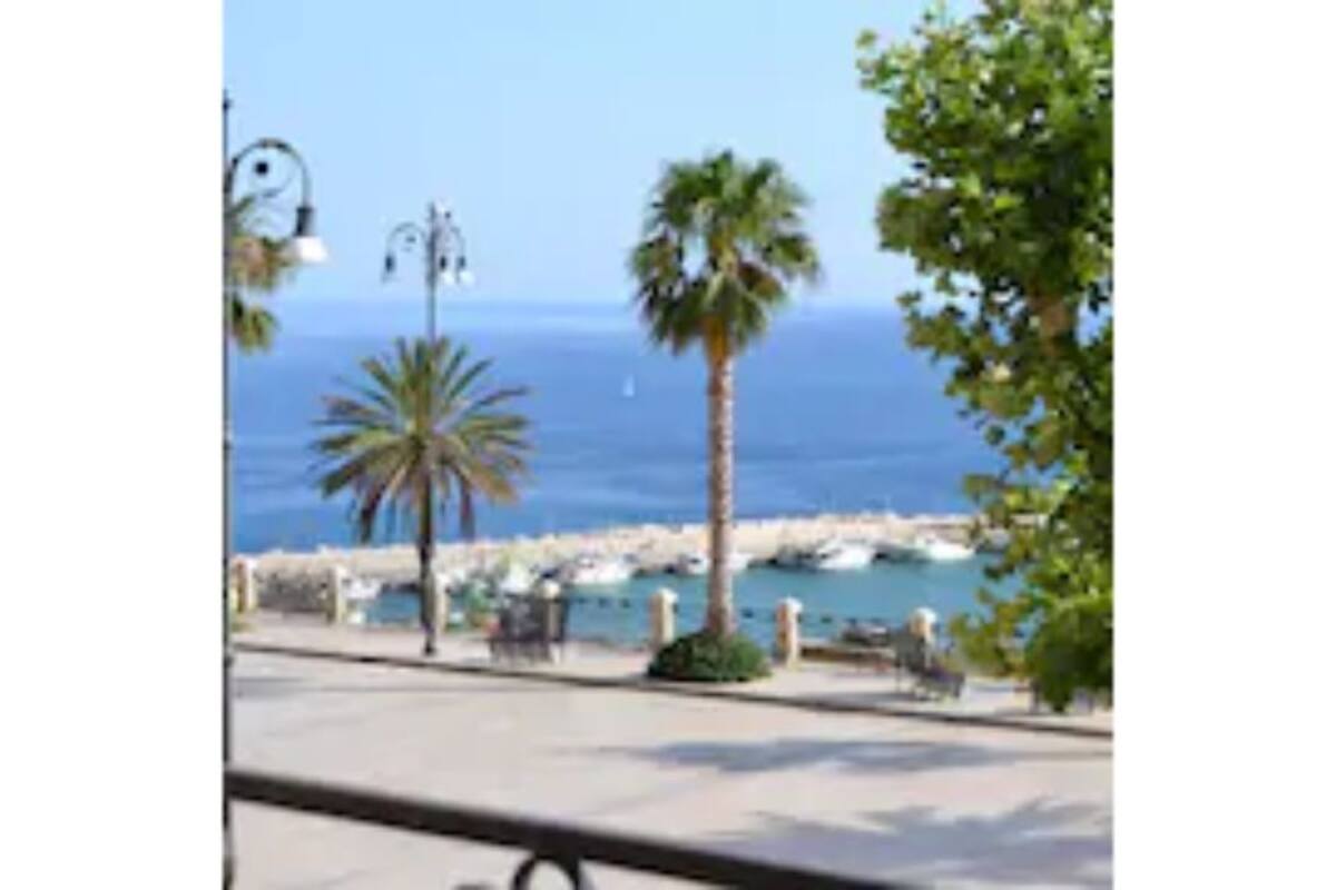 A coastal promenade with a view of the sea, palm trees, and a row of beachside buildings.