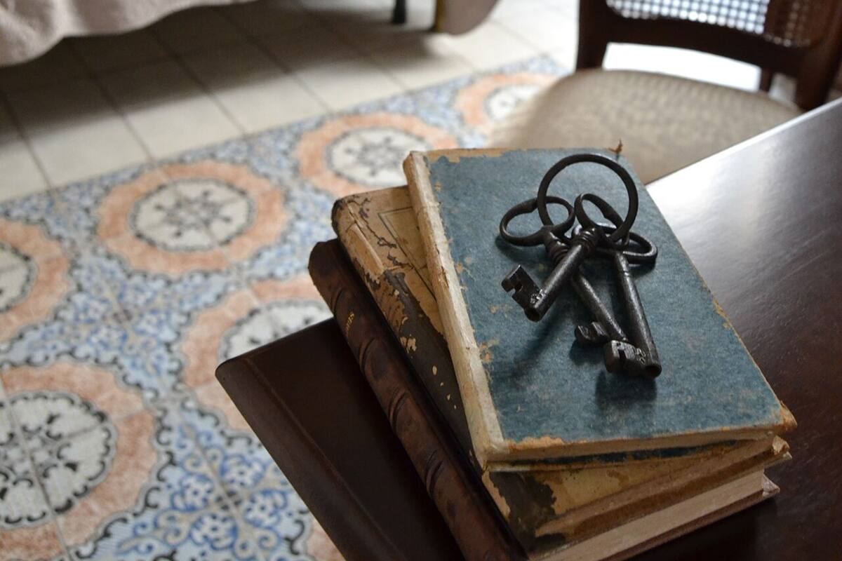 A room with a bed, a chair, and a table with books and a key.