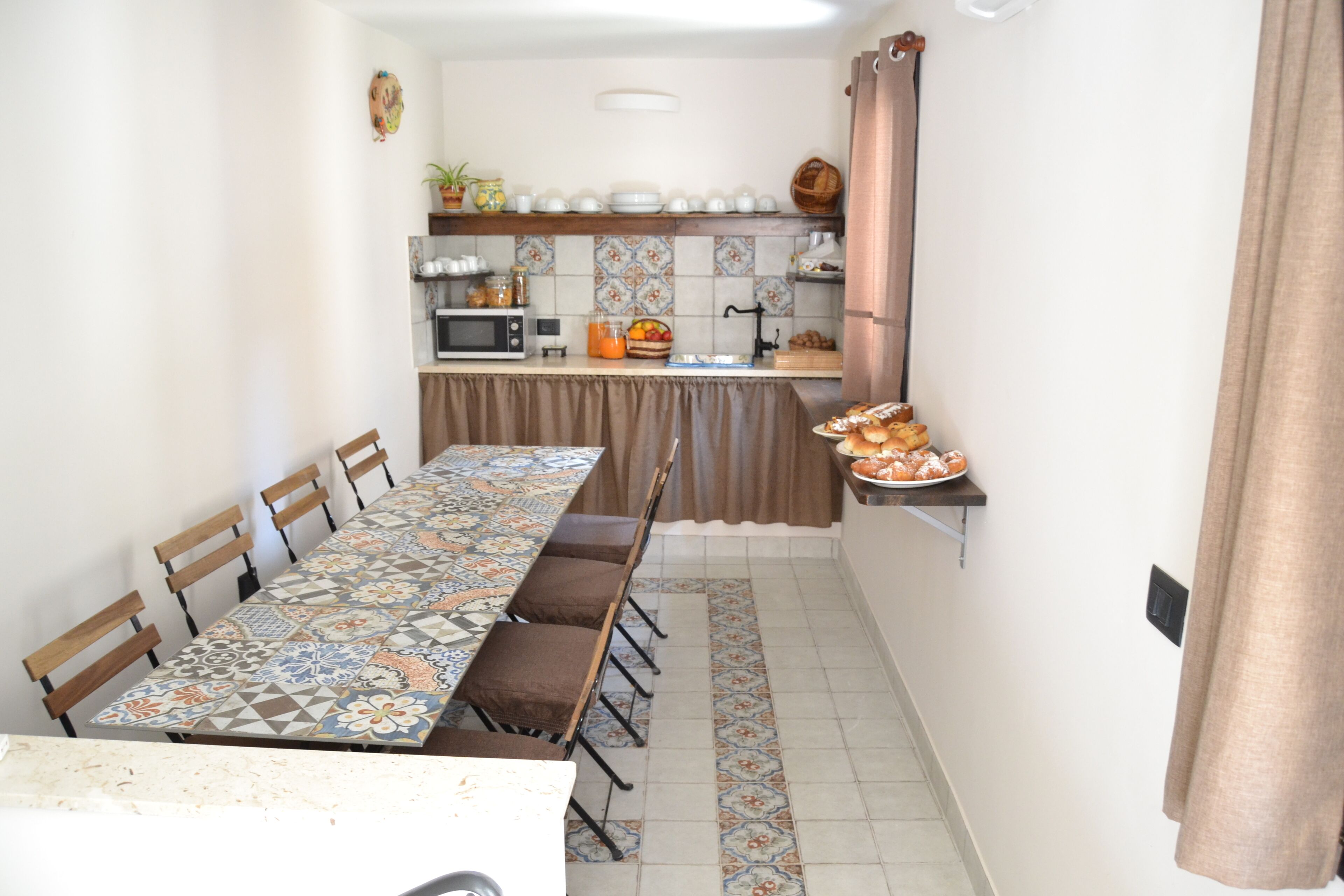 A dining area with a long table, chairs, and a kitchen in the background.
