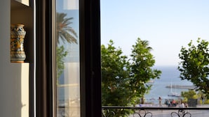 A window with a decorative vase and a view of a coastal area with trees and a body of water. - Agorà Panoramic Rooms (Sciacca)