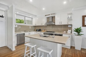 A modern kitchen with white cabinetry, a central island with bar stools, a stainless steel range hood, and a window with a view of greenery.