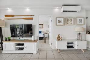 A modern living room with a flat-screen TV, white cabinetry, and a dining area with a wooden table.