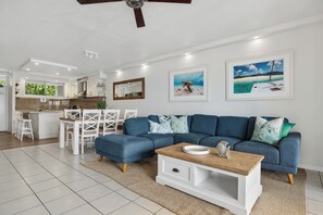 A modern living room with a sectional sofa, a coffee table, and a dining area with white chairs.