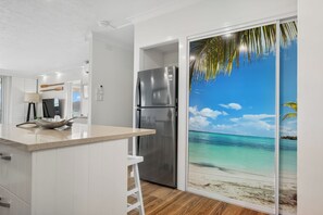 A kitchen with a stainless steel refrigerator, a bar counter, and a view of a beach through a sliding door.