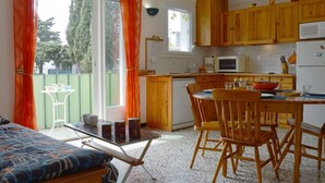 A compact kitchen with wooden cabinets, a dining table with chairs, a microwave, and a refrigerator. - Cozy Apartment with Parking, 100m from Beach - Argelès-sur-Mer (Argelès-sur-Mer)