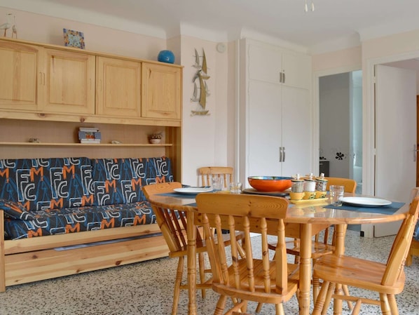 A cozy dining area with a wooden table and chairs, a patterned sofa, and wooden cabinets. - Cozy Apartment with Parking, 100m from Beach - Argelès-sur-Mer (Argelès-sur-Mer)