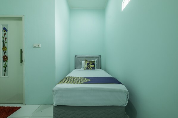 A narrow room with a bed, a door with a floral decoration, and a thermostat on the wall. - OYO Life 1889 Mbuahpage (Karawang)